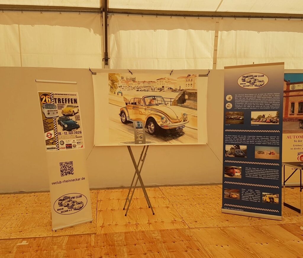 Gemälde eines gelben VW Käfers auf einer Staffelei zwischen zwei Informations-Rollups in einem Ausstellungszelt.